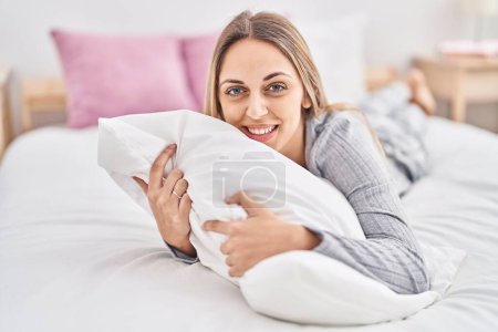 Photo for Young woman hugging pillow lying on bed at bedroom - Royalty Free Image
