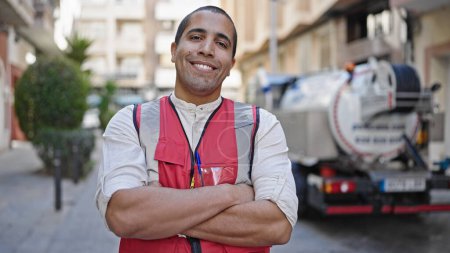 Téléchargez les photos : Jeune homme hispanique volontaire souriant vêtu d'un gilet dans la rue - en image libre de droit