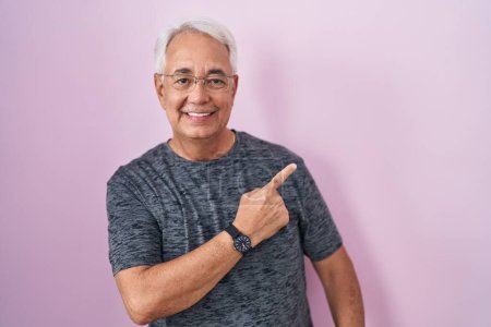 Photo for Middle age man with grey hair standing over pink background cheerful with a smile on face pointing with hand and finger up to the side with happy and natural expression - Royalty Free Image