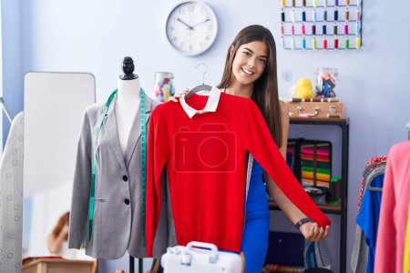 Photo for Young beautiful hispanic woman tailor smiling confident holding t shirt at tailor shop - Royalty Free Image