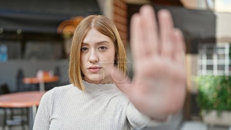 Foto de Mujer rubia joven haciendo gesto de parada con la mano en la terraza de la cafetería - Imagen libre de derechos