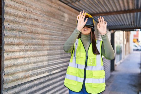 Téléchargez les photos : Jeune belle architecte hispanique utilisant des lunettes de réalité virtuelle à la rue - en image libre de droit