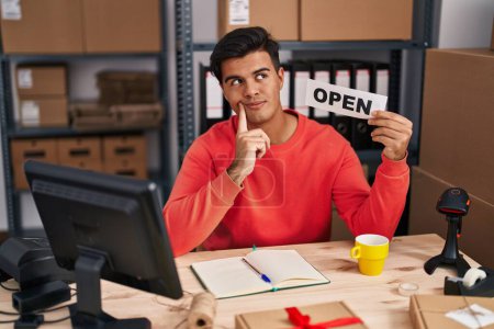 Photo for Hispanic man working at small business ecommerce holding open banner serious face thinking about question with hand on chin, thoughtful about confusing idea - Royalty Free Image