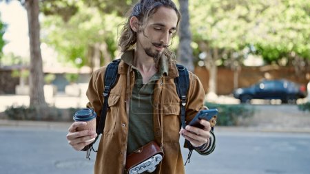 Téléchargez les photos : Jeune homme hispanique touriste en utilisant smartphone tenant café au parc - en image libre de droit