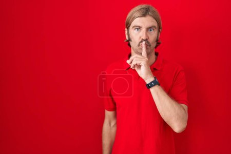 Téléchargez les photos : Homme caucasien avec moustache debout sur fond rouge demandant à être calme avec le doigt sur les lèvres. silence et concept secret. - en image libre de droit