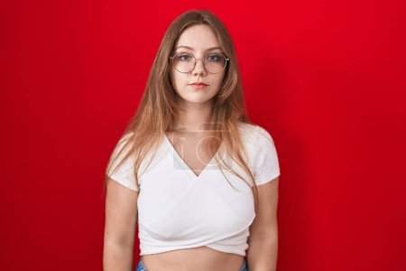 Photo for Young caucasian woman standing over red background relaxed with serious expression on face. simple and natural looking at the camera. - Royalty Free Image