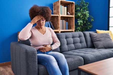Téléchargez les photos : Femme afro-américaine malade assis sur le canapé à la maison - en image libre de droit