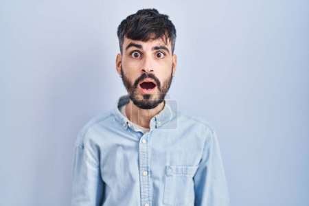 Photo for Young hispanic man with beard standing over blue background afraid and shocked with surprise and amazed expression, fear and excited face. - Royalty Free Image