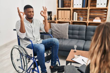 Foto de Hombre afroamericano haciendo terapia sentado en silla de ruedas relajarse y sonreír con los ojos cerrados haciendo gesto de meditación con los dedos. concepto de yoga. - Imagen libre de derechos