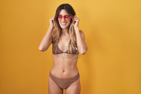 Photo for Young hispanic woman wearing bikini over yellow background covering ears with fingers with annoyed expression for the noise of loud music. deaf concept. - Royalty Free Image