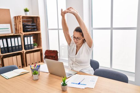 Photo for Young beautiful hispanic woman business worker using laptop stretching arms at office - Royalty Free Image