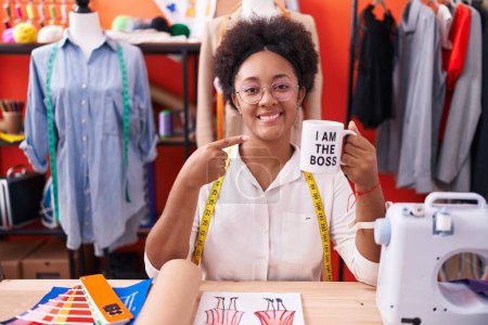 Photo for Beautiful african woman with curly hair dressmaker designer drinking from i am the boss cup smiling happy pointing with hand and finger - Royalty Free Image