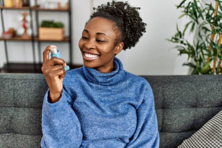 Téléchargez les photos : Femme afro-américaine utilisant inhalateur assis sur le canapé à la maison - en image libre de droit