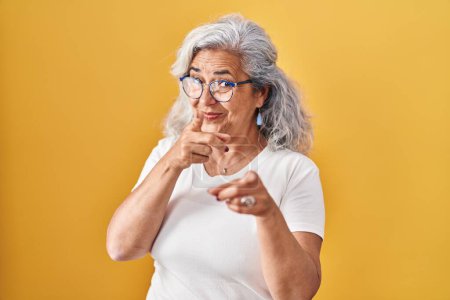Téléchargez les photos : Middle age woman with grey hair standing over yellow background pointing fingers to camera with happy and funny face. good energy and vibes. - en image libre de droit