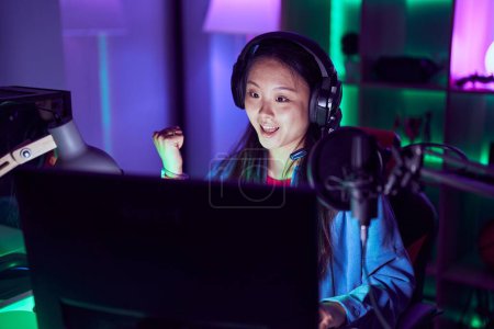 Téléchargez les photos : Jeune femme asiatique jouer à des jeux vidéo pointant pouce vers le côté souriant heureux avec bouche ouverte - en image libre de droit