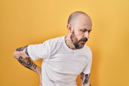 Photo for Young hispanic man with tattoos standing over yellow background suffering of backache, touching back with hand, muscular pain - Royalty Free Image