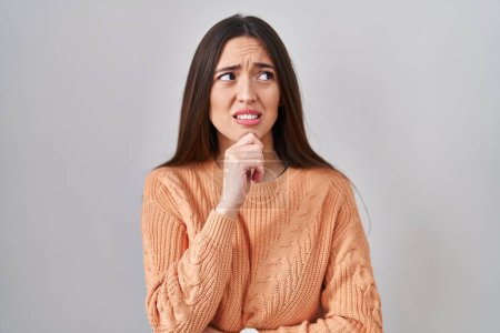 Téléchargez les photos : Jeune femme brune debout sur fond blanc pensant inquiet d'une question, préoccupé et nerveux avec la main sur le menton - en image libre de droit