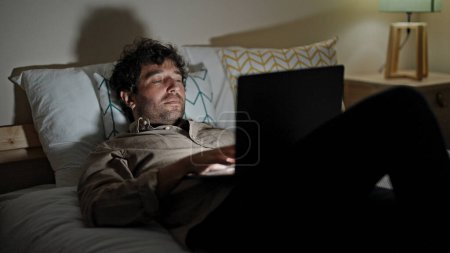 Photo for Young hispanic man using laptop lying on bed working at bedroom - Royalty Free Image