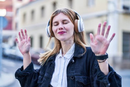 Foto de Young blonde woman listening to music and dancing at street - Imagen libre de derechos