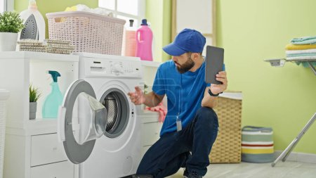 Photo for Young hispanic man technician repairing washing machine holding touchpad at laundry room - Royalty Free Image
