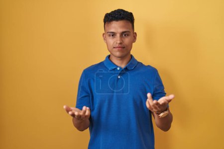 Photo for Young hispanic man standing over yellow background clueless and confused with open arms, no idea concept. - Royalty Free Image