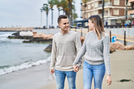 Foto de Hombre y mujer pareja sonriendo confiado caminando con las manos juntas en la playa - Imagen libre de derechos