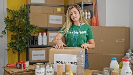 Téléchargez les photos : Jeune femme blonde emballage bénévole boîte en carton pour faire un don au centre de charité - en image libre de droit