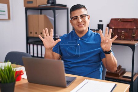 Téléchargez les photos : Jeune homme hispanique travaillant au bureau avec ordinateur portable montrant et pointant vers le haut avec les doigts numéro neuf tout en souriant confiant et heureux. - en image libre de droit