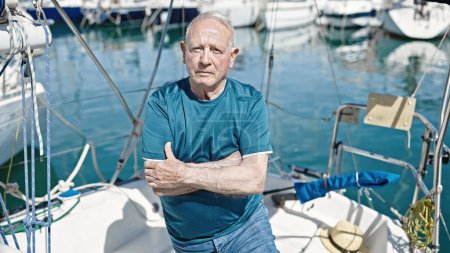Téléchargez les photos : Homme âgé aux cheveux gris debout avec une expression détendue et les bras croisés geste au bateau - en image libre de droit