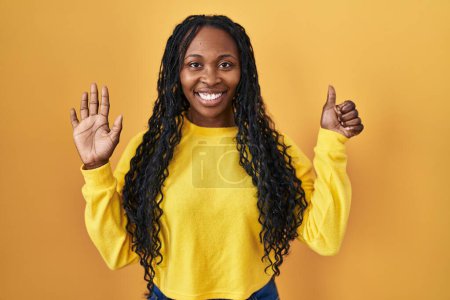 Téléchargez les photos : Femme africaine debout sur fond jaune montrant et pointant vers le haut avec les doigts numéro six tout en souriant confiant et heureux. - en image libre de droit