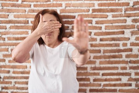 Photo for Senior woman with glasses standing over bricks wall covering eyes with hands and doing stop gesture with sad and fear expression. embarrassed and negative concept. - Royalty Free Image