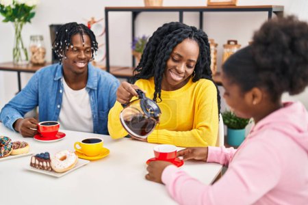 Téléchargez les photos : Amis afro-américains prenant le petit déjeuner assis sur la table à la maison - en image libre de droit
