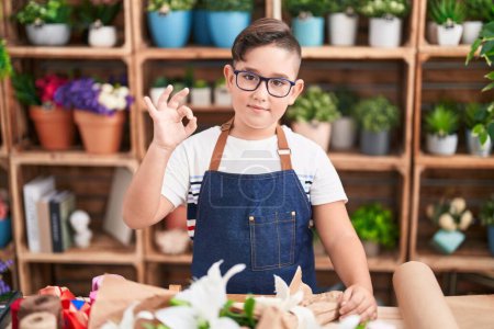 Téléchargez les photos : Jeune hispanique enfant travaillant à la boutique de fleuriste faire ok signe avec les doigts, sourire geste amical excellent symbole - en image libre de droit