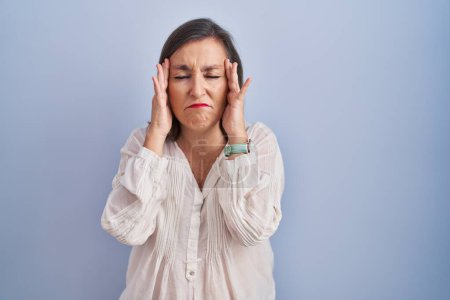 Foto de Mujer hispana de mediana edad de pie sobre fondo azul con la mano en la cabeza, dolor de cabeza porque el estrés. padecer migraña. - Imagen libre de derechos