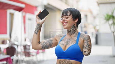 Photo for Hispanic woman with amputee arm dancing listening to music on smartphone at coffee shop terrace - Royalty Free Image