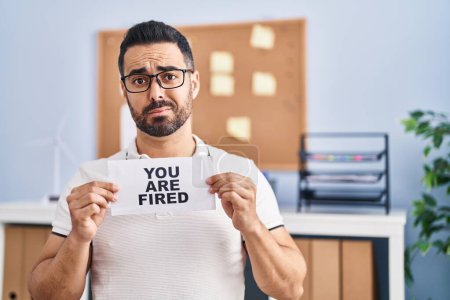 Photo for Young hispanic man with beard holding you are fired banner at the office skeptic and nervous, frowning upset because of problem. negative person. - Royalty Free Image