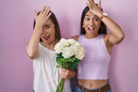 Photo for Hispanic mother and daughter holding bouquet of white flowers surprised with hand on head for mistake, remember error. forgot, bad memory concept. - Royalty Free Image