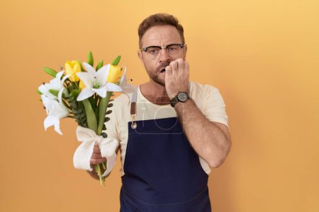 Photo for Middle age man with beard florist shop holding flowers looking stressed and nervous with hands on mouth biting nails. anxiety problem. - Royalty Free Image