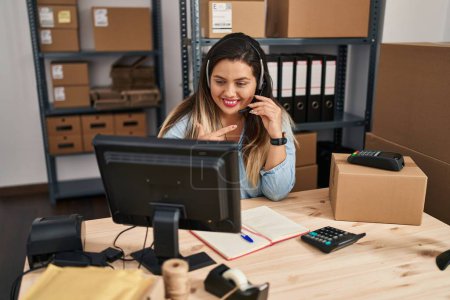 Photo for Young hispanic woman working at small business ecommerce wearing headset smiling happy pointing with hand and finger - Royalty Free Image