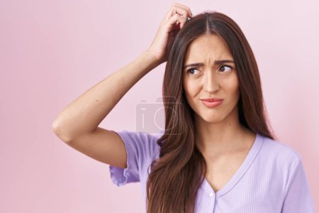 Téléchargez les photos : Jeune femme hispanique avec les cheveux longs debout sur fond rose confondre et se poser des questions. incertain avec doute, pensant la main sur la tête. concept coûteux. - en image libre de droit