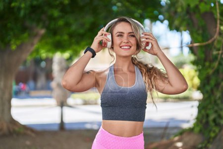 Foto de Mujer rubia joven usando ropa deportiva escuchando música en el parque - Imagen libre de derechos