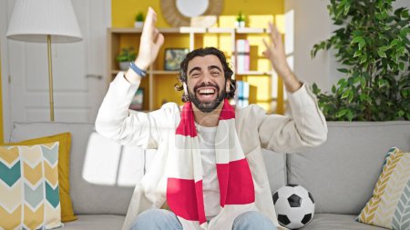 Photo for Young hispanic man watching soccer match celebrating at home - Royalty Free Image