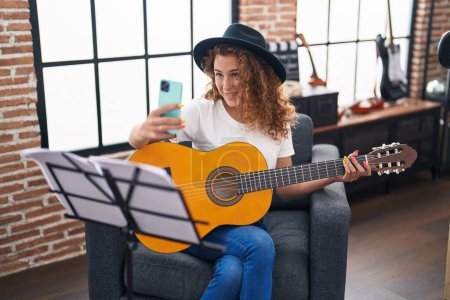 Téléchargez les photos : Jeune belle musicienne hispanique jouant de la guitare classique faire selfie par smartphone au studio de musique - en image libre de droit