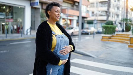Foto de Joven embarazada sonriendo confiado tocando vientre en la calle - Imagen libre de derechos