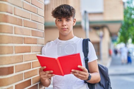 Photo for Young hispanic teenager student wearing backpack reading book at street - Royalty Free Image
