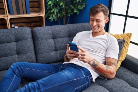 Photo for Young man using smartphone lying on sofa at home - Royalty Free Image