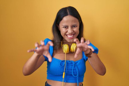 Photo for Hispanic young woman standing over yellow background smiling funny doing claw gesture as cat, aggressive and sexy expression - Royalty Free Image