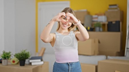 Téléchargez les photos : Jeune femme blonde faisant un geste de coeur à la nouvelle maison - en image libre de droit