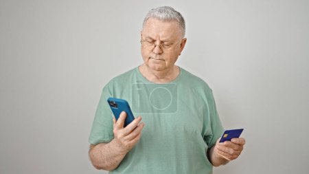 Foto de Hombre de pelo gris de mediana edad de compras con teléfono inteligente y tarjeta de crédito sobre fondo blanco aislado - Imagen libre de derechos