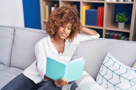 Photo for African american woman reading book sitting on sofa at home - Royalty Free Image